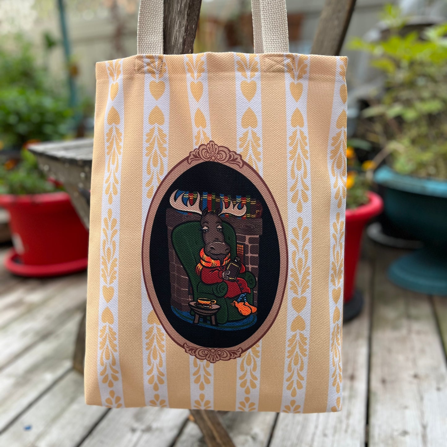 Tote bag with decorative design of a person in a chair on a wooden surface with plants in the background